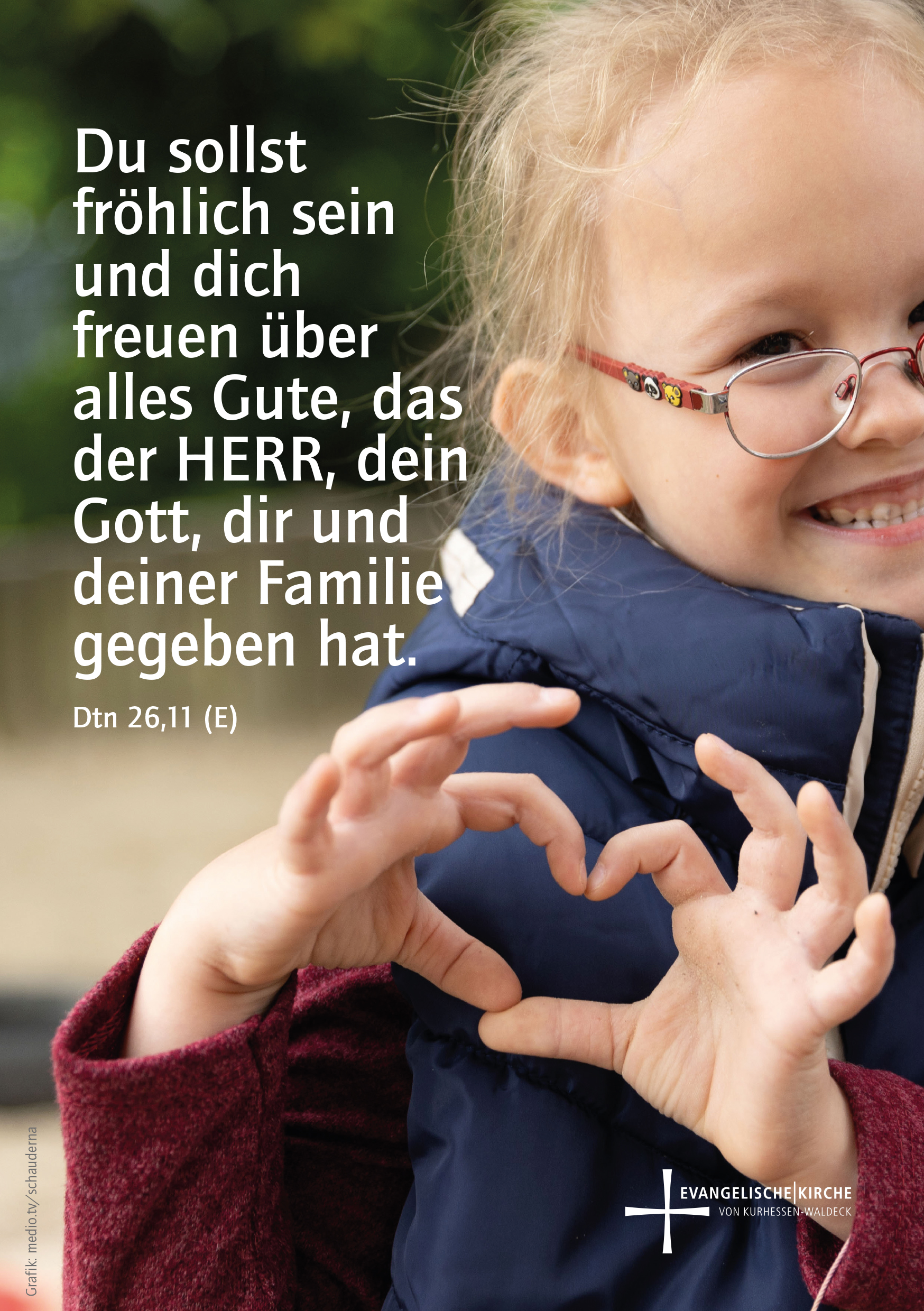 Monatsspruch Februar 2026. Ein kleines Mädchen mit Brille lacht und macht ein Herz mit ihren Händen.