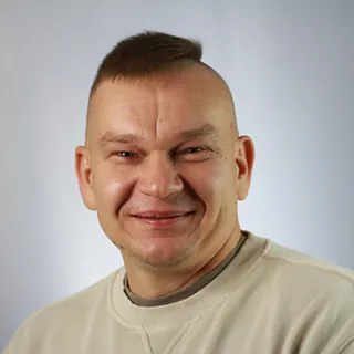 Porträtfoto von Pfarrer Ivan Shirokov vor hellem Hintergrund. Er trägt ein helles Sweatshirt und lächelt in die Kamera.